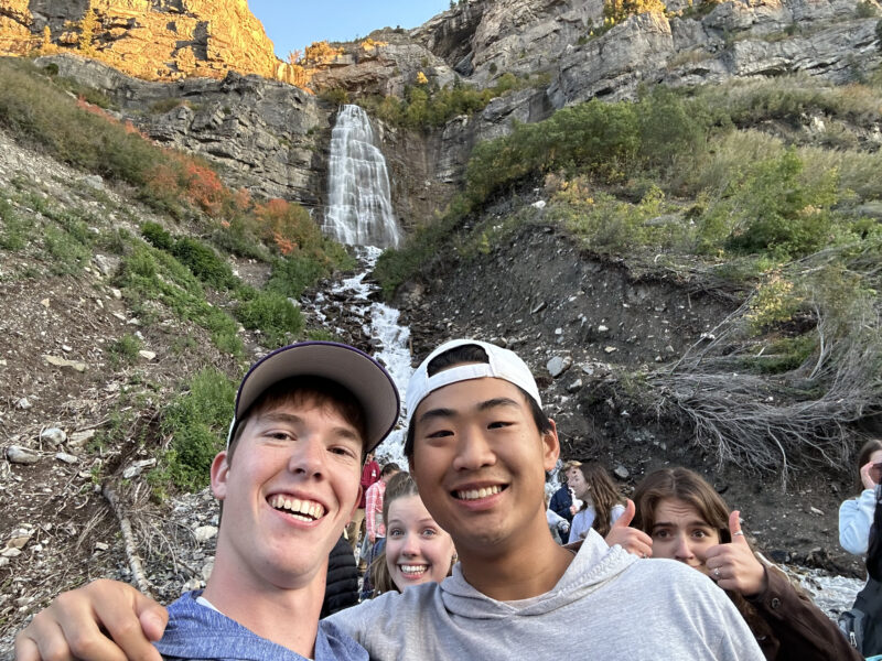 Two young Gen Z Men standing in front of a waterfall in Utah enjoying in-person community and Christ-centered relationships