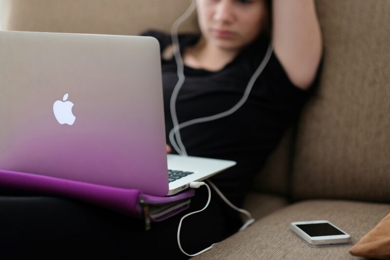 Girl sitting on couch with her headphones in staring at laptop screen disconnected from community.